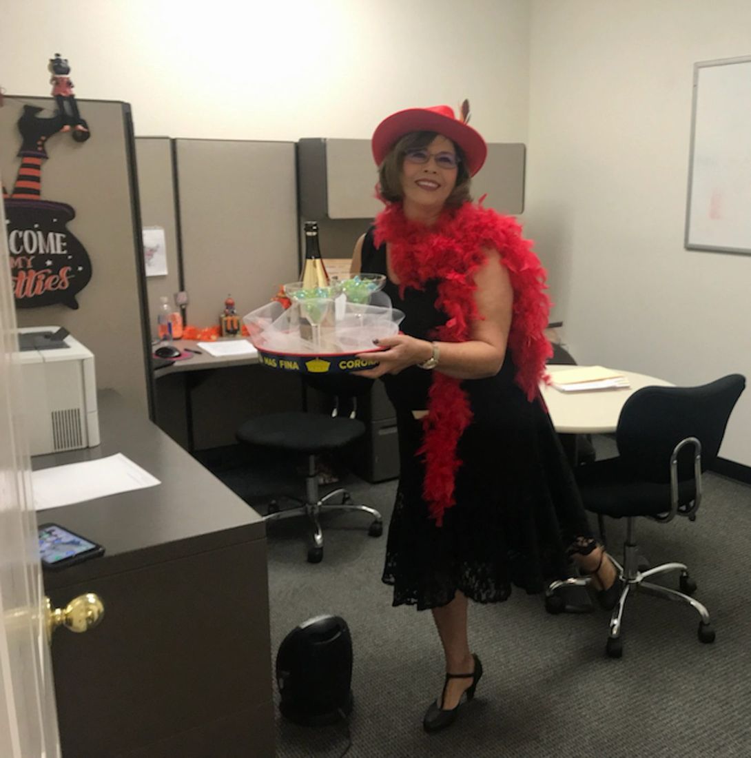 Sylvia in Halloween attire at the office, holding a drink tray