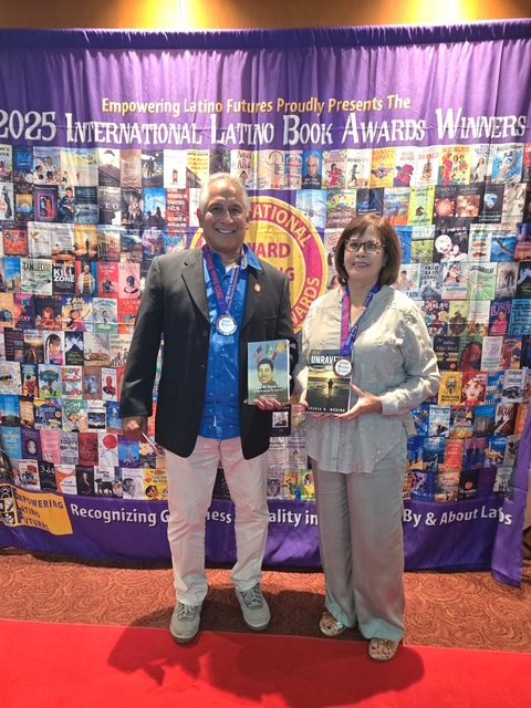 Sylvia holding Unraveled and wearing her medal in front of the 2025 International Latino Book Awards winners wall