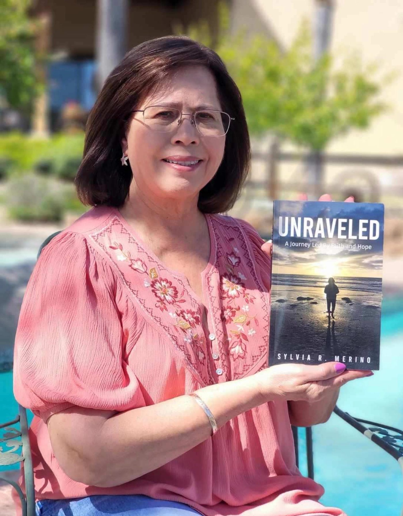 Sylvia Merino holding her book Unraveled beside a pool